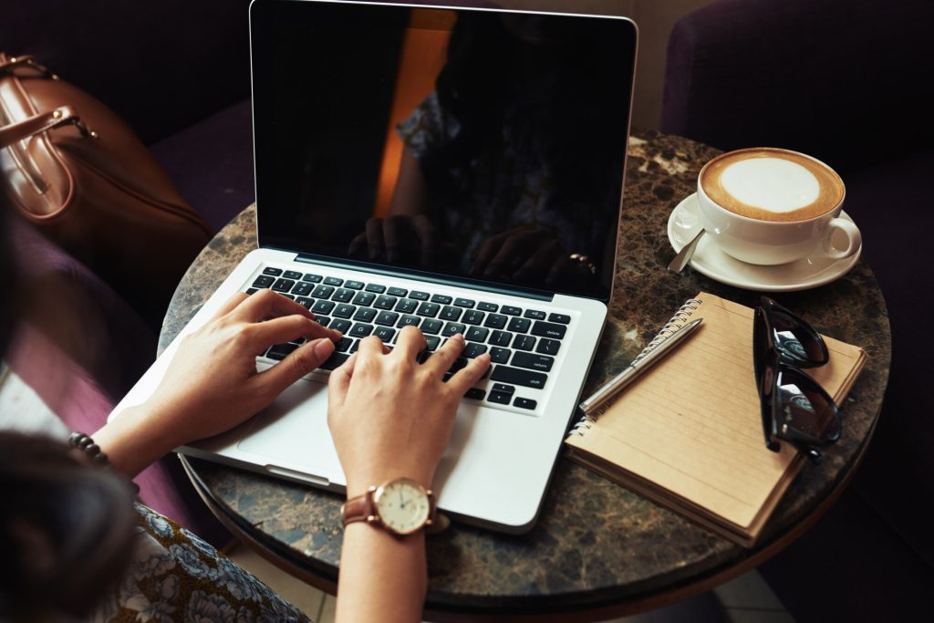 Handen van een onherkenbare vrouw die typt op een laptop in een café.
