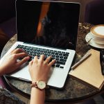 Handen van een onherkenbare vrouw die typt op een laptop in een café.