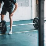 man in black t-shirt and black shorts holding black barbell